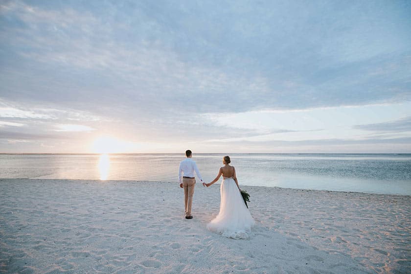bride and groom walk on beach hand in hand