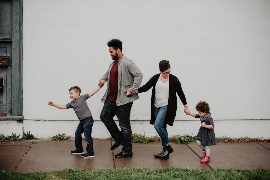 family of four walking on sidewalk holding hands with the young boy leading the way, followed by dad, mom, and young girl.